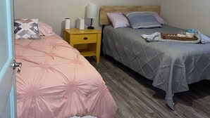 A bedroom with two beds, wooden flooring, a ceiling fan, and a nightstand with a lamp. - Lovely Beach View, 2 BR Condo (Corpus Christi)