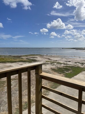 A wooden deck overlooking a beach with a clear sky and distant shoreline. - Lovely Beach View, 2 BR Condo (Corpus Christi)