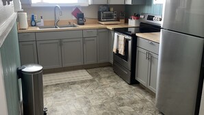 A kitchen with grey cabinets, a stainless steel refrigerator, a microwave, and a stove. - Lovely Beach View, 2 BR Condo (Corpus Christi)