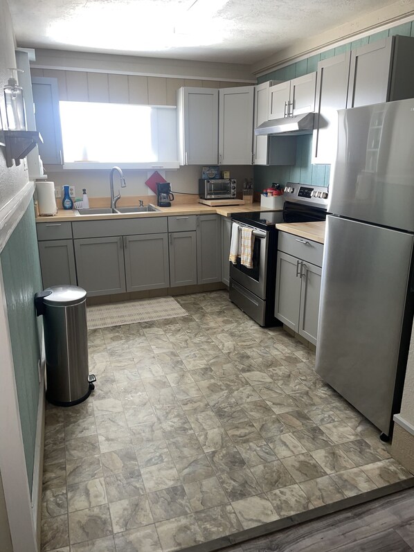 A kitchen with grey cabinets, a stainless steel refrigerator, a microwave, and a stove. - Lovely Beach View, 2 BR Condo (Corpus Christi)