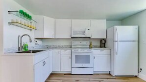Une cuisine avec des meubles blancs, un four à micro-ondes, une cuisinière et un réfrigérateur.