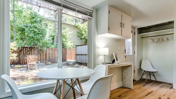 Une cuisine moderne avec un coin repas, comprenant une table ronde et des chaises, un banc intégré et une vue sur le jardin à travers de grandes portes-fenêtres coulissantes.