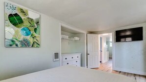 Une chambre à coucher comprenant un lit, une commode blanche, une armoire blanche et une porte donnant sur une autre pièce.
