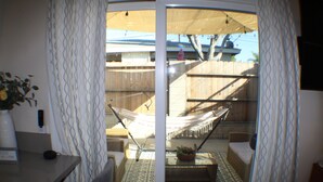 A room with a sliding glass door leading to an outdoor area with a hammock, a wooden deck, and a potted plant.