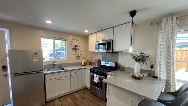 A modern kitchen with white cabinets, stainless steel appliances, a wooden floor, and a window with a view of the outside.