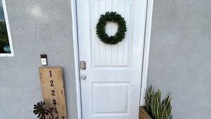 A white door with a wreath, a wooden number sign, a doormat, and a planter.