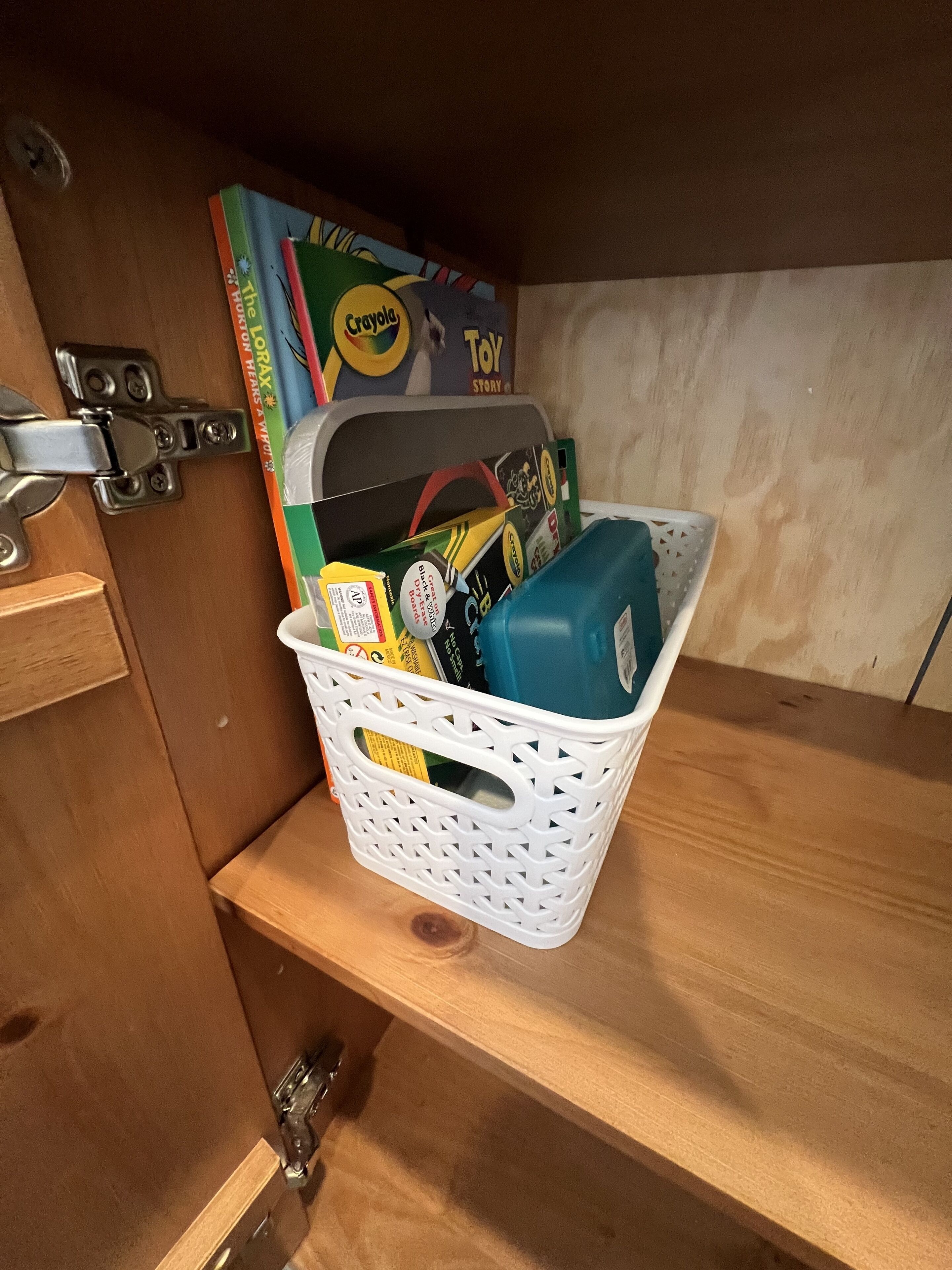 A white plastic basket filled with various items, including a blue water bottle, on a wooden shelf.