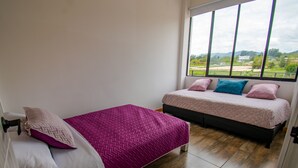 A bedroom with two beds, one with a pink bedspread and the other with a white bedspread. There is a large window providing a view of the outdoors. - El Roble Hotel Boutique (Paipa)