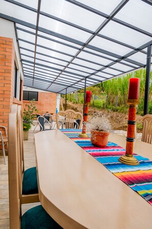 Une terrasse extérieure avec une table dressée pour le repas, entourée de chaises, et une plante en pot.