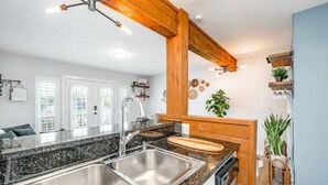 Une cuisine dotée de plans de travail en granit, d’éviers en acier inoxydable, de poutres en bois et d’un four encastré.