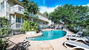 Un espace piscine avec des chaises longues, un bâtiment en pierre et une terrasse clôturée.