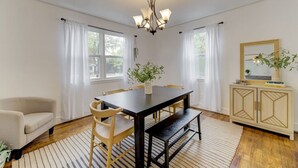 Un coin repas avec une table en bois foncé, des chaises de couleur beige, un lustre et un meuble agrémenté d’un miroir et d’une plante.