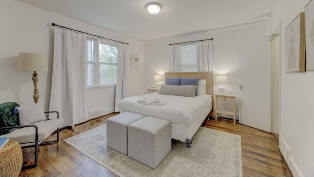 Une chambre à coucher avec un lit, des tables de chevet, une lampe, une chaise et une fenêtre avec des rideaux.