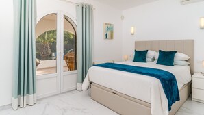 A bedroom with a bed, a nightstand, a wall-mounted light, and a view through a glass door. - 2 Bedroom Villa in Landscaped Gardens (Javea / Xàbia)