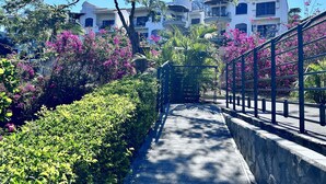 A pathway leading to a building with balconies, surrounded by lush greenery and pink flowers. - EXCLUSIVE LA PERLA TAMARINDO CONDO 3BR LUXURY RETREAT, WALK TO BEACH AND DINING! (Tamarindo)