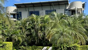 A swimming pool with lounge chairs, surrounded by palm trees and a modern building with a cylindrical water tank. - EXCLUSIVE LA PERLA TAMARINDO CONDO 3BR LUXURY RETREAT, WALK TO BEACH AND DINING! (Tamarindo)