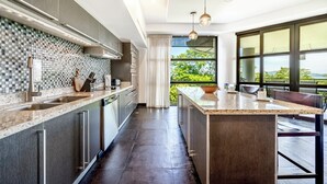 A modern kitchen with a large island, stainless steel appliances, and a view of greenery through large windows. - EXCLUSIVE LA PERLA TAMARINDO CONDO 3BR LUXURY RETREAT, WALK TO BEACH AND DINING! (Tamarindo)