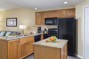 A kitchen with wooden cabinets, a black refrigerator, a microwave, and a granite countertop. - 1BD Deluxe/Branson - Pools, Gym, BBQ, Game Room! (Branson)
