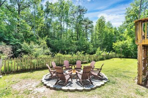 A circular outdoor seating area with Adirondack chairs around a fire pit, surrounded by a wooden deck and a wooden fence.
