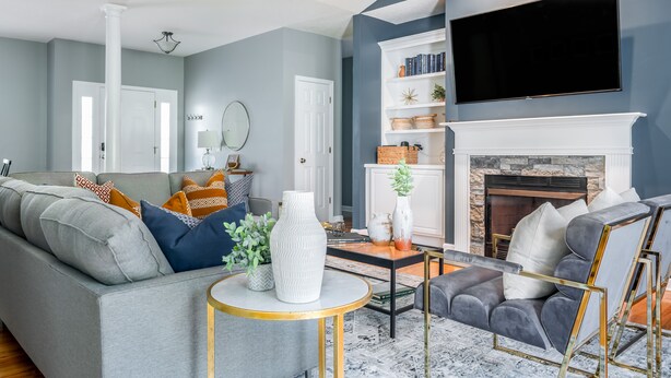 Een moderne woonkamer met een grijze bank, een grijze fauteuil, een ronde salontafel en een open haard.