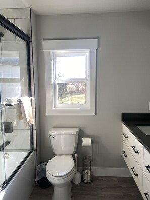 Ein modernes Badezimmer mit Toilette, Fenster, Duschkabine aus Glas und Holzboden.