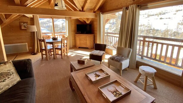L’intérieur chaleureux d’un chalet en bois comprend un coin repas, un canapé et un balcon offrant une vue sur les montagnes.
