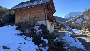 Un chalet en bois, doté d’un toit en pente, entouré de paysages enneigés et avec des montagnes en arrière-plan.