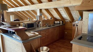 Une cuisine en bois avec un plafond en pente, un four à micro-ondes encastré, un évier et une poubelle.