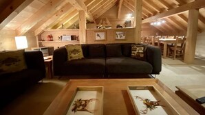 Une chambre mansardée avec des poutres en bois, un canapé, une table basse et un bureau avec un ordinateur.