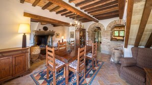 Un comedor rústico con mesa y sillas de madera, chimenea y arcos de piedra.