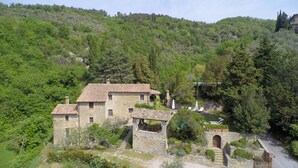 Un edificio de piedra con tejado de tejas, rodeado de abundante vegetación y una ladera.