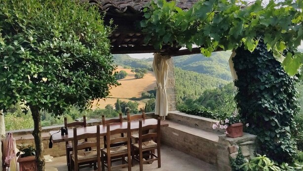 Una mesa y sillas de madera bajo una pérgola con vistas a un valle.
