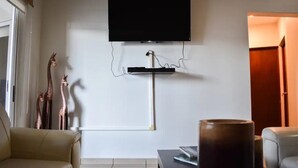 Una sala de estar con una televisión de pantalla plana montada en la pared, un sofá, una mesa de centro y un jarrón decorativo.