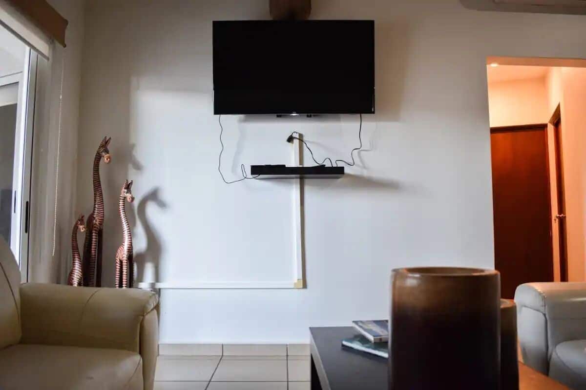 A living room with a flat-screen TV mounted on the wall, a sofa, a coffee table, and a decorative vase.