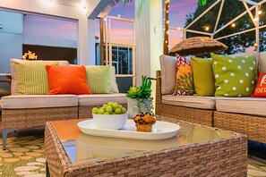 A cozy seating area with a wicker table, a bowl of green grapes, a pineapple, and a muffin.