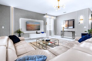 A modern living room with a sofa set, a coffee table, a TV mounted on the wall, and a fireplace.