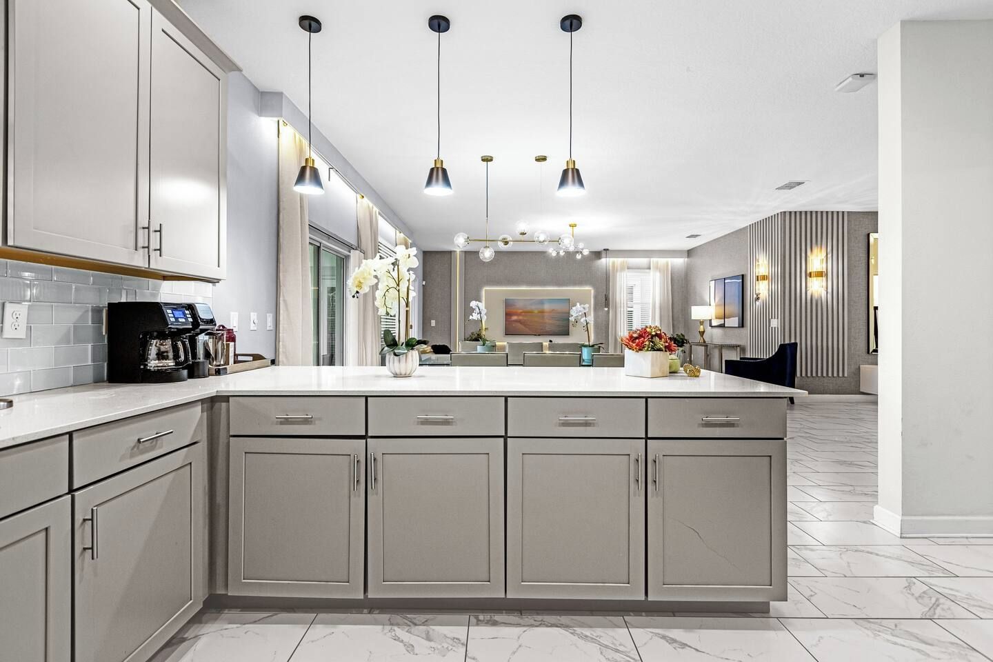 Une cuisine moderne dotée d’un grand îlot central, de luminaires suspendus et donnant sur la salle à manger.