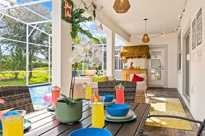 An outdoor patio area with a pool, wicker furniture, and a thatched roof structure.