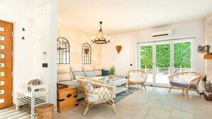 Un vaste espace de vie comprenant un canapé, deux fauteuils en osier, une table basse et un lustre.