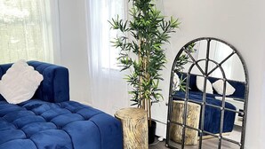 Un salon moderne avec un canapé bleu, une grande plante en pot, un miroir rond et un tabouret en bois.
