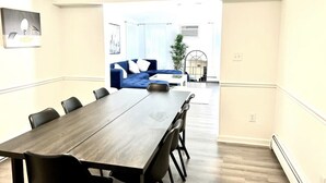 Un espace repas moderne avec une longue table et des chaises, un canapé bleu et une plante en arrière-plan.