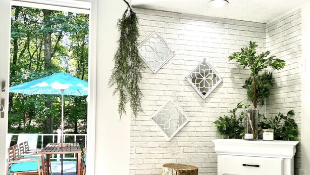 Une pièce avec un mur en briques blanches, une table et des chaises en bois, une plante suspendue et une commode blanche.