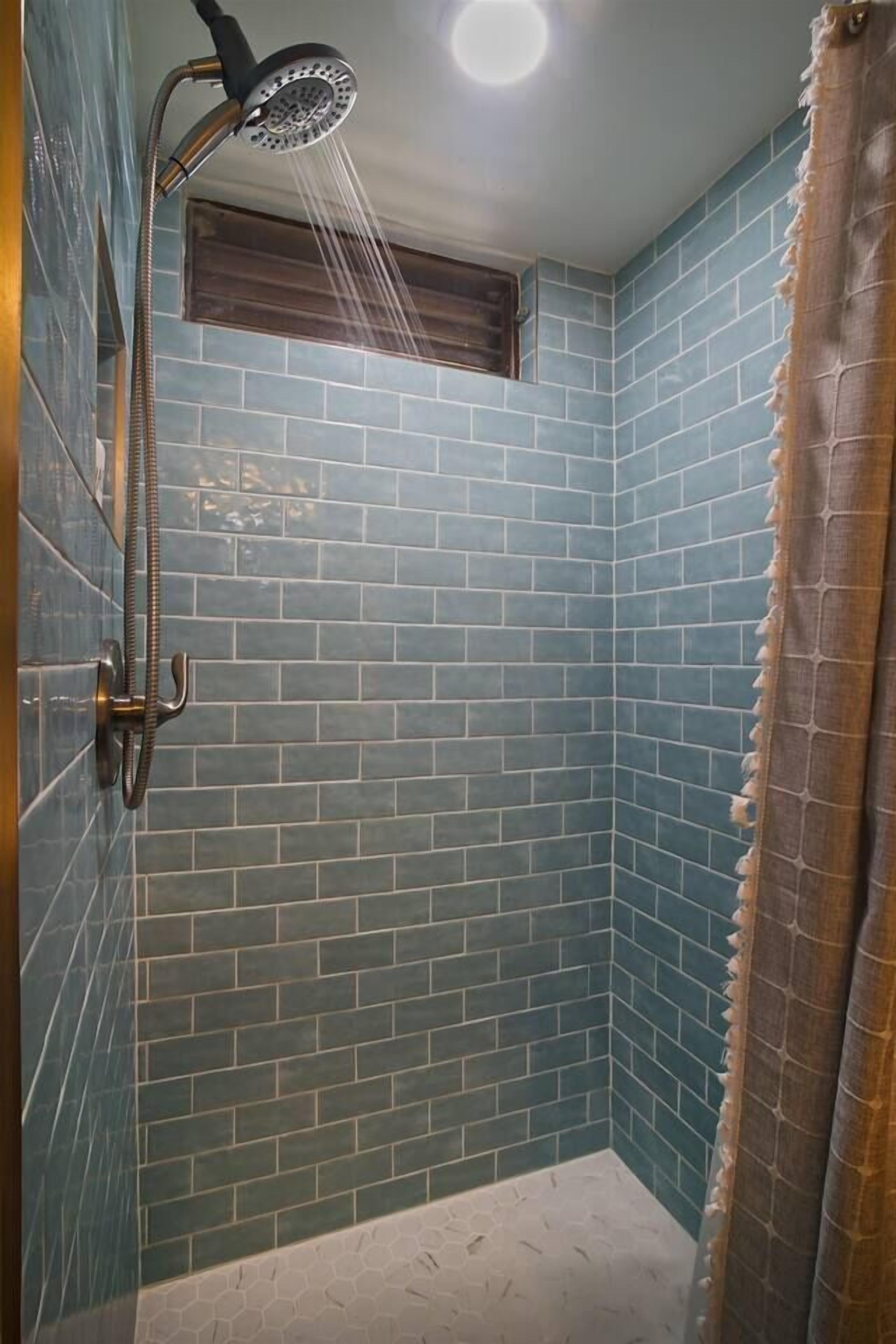 A shower with a handheld showerhead and a wall-mounted faucet, tiled in a blue pattern.