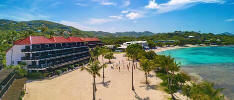 A beachfront hotel with multiple balconies, a sandy beach, and a clear view of the turquoise sea.