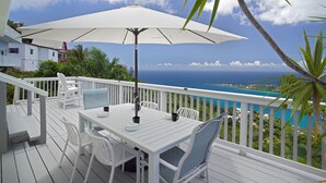 Une terrasse blanche avec une table et des chaises, un grand parasol et une vue sur l’océan.