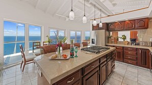 A modern kitchen with a large island, wooden cabinets, and a view of the ocean. - Private Pool, Sun Deck, Cliffside, Ocean Views, AC (St. Thomas)
