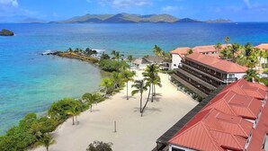 A beachfront hotel with a pool, palm trees, and a view of the ocean and mountains. - Beachfront, Corner Unit Sapphire, Restaurants, Pool (St. Thomas)