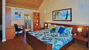 A bedroom with a large bed, a desk, and a chair. There is a painting on the wall and a door leading to another room. - Beachfront, Corner Unit Sapphire, Restaurants, Pool (St. Thomas)