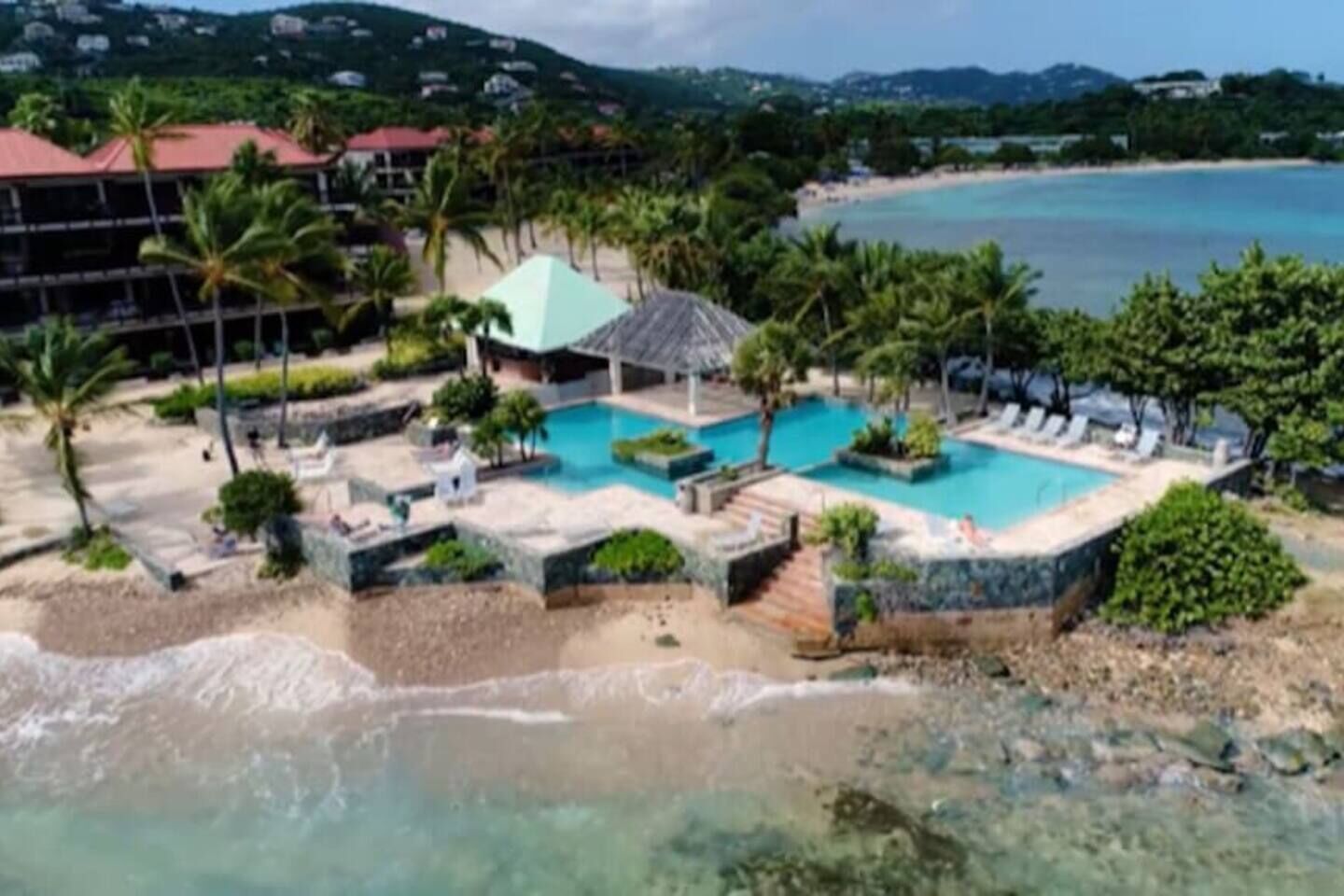 A resort with a pool, beach, and mountains in the background.