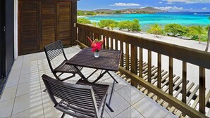 A balcony with a table and chairs, overlooking a turquoise sea and a distant island. - Beachfront, Corner Unit Sapphire, Restaurants, Pool (St. Thomas)
